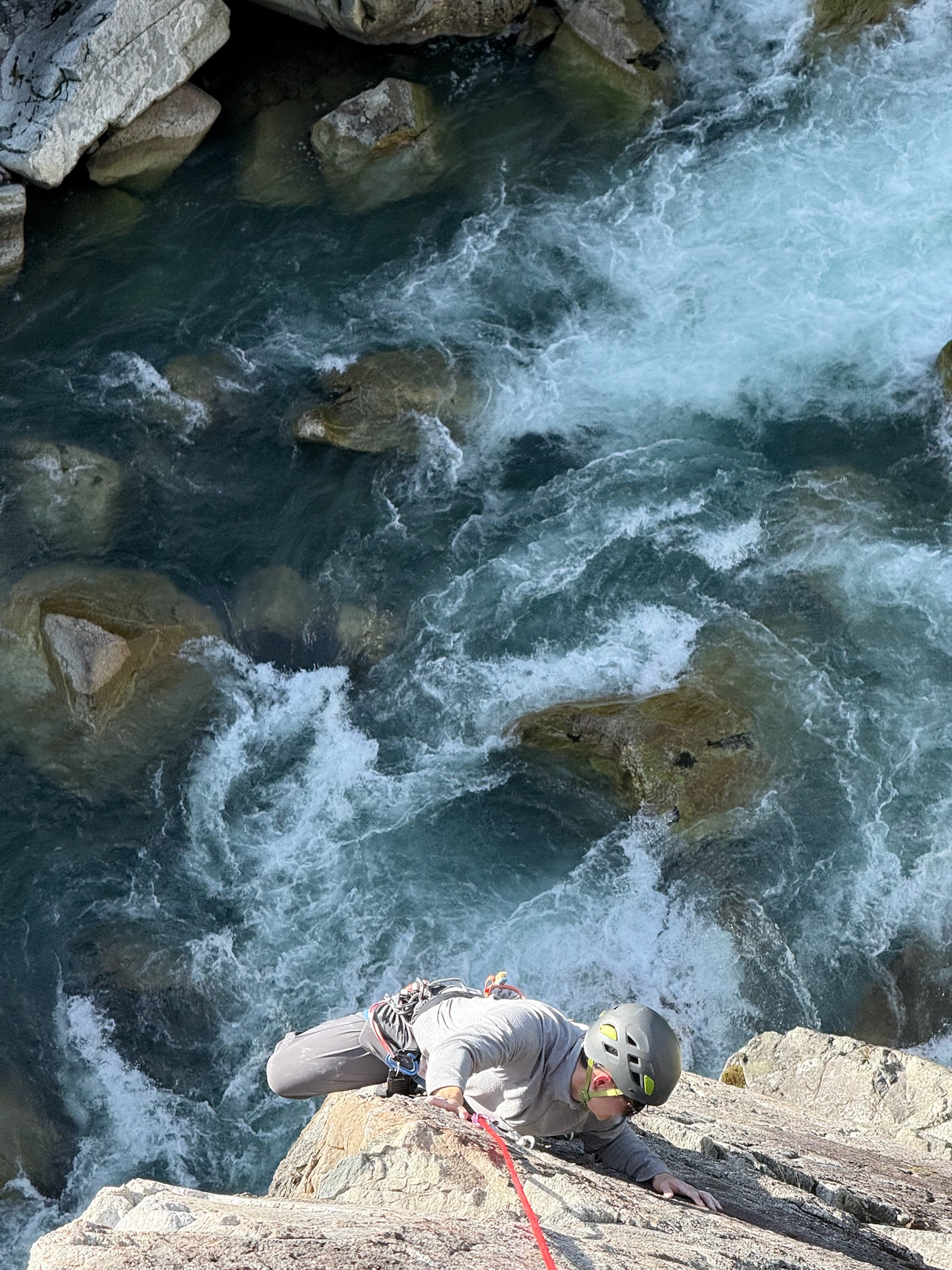 Rock climber scaling a cliff above river rapids